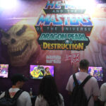 Participants jouant à des jeux vidéo lors de la Gamescom 2026, avec un grand affichage de He-Man et des personnages de Masters of the Universe.