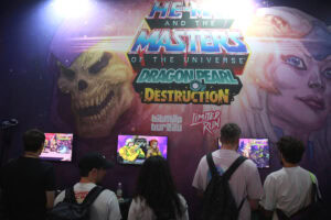Participants jouant à des jeux vidéo lors de la Gamescom 2026, avec un grand affichage de He-Man et des personnages de Masters of the Universe.