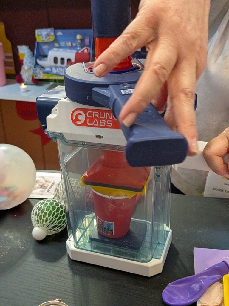 Une personne utilise un appareil CrunchLabs pour tester une expérience scientifique avec un liquide coloré dans un environnement de magasin de jouets.