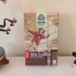 Jeu de société Crime Zoom : Sous le vernis, en édition de poche, présenté avec des figurines de jouets sur une table.