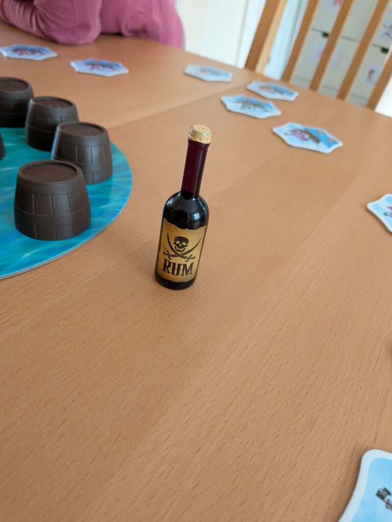 Bouteille de rhum miniature sur une table de jeu de société avec des cartes et des gobelets en plastique.