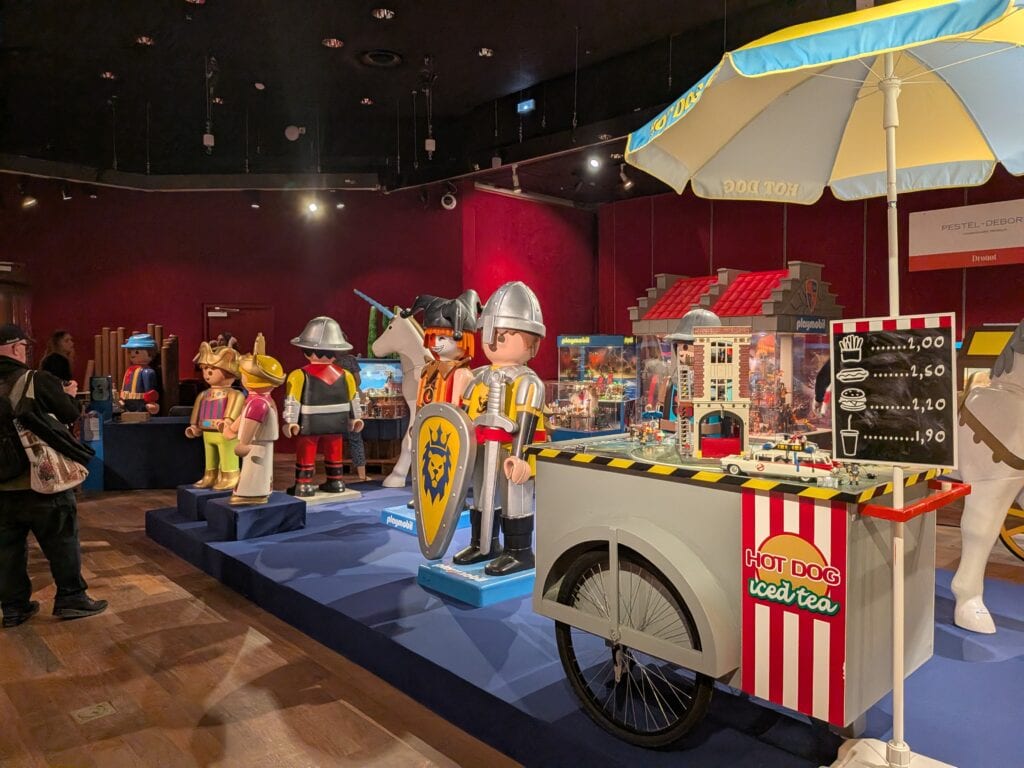 Exposition de figurines Playmobil avec personnages médiévaux, châteaux et stands de vente dans une salle d'exposition.
