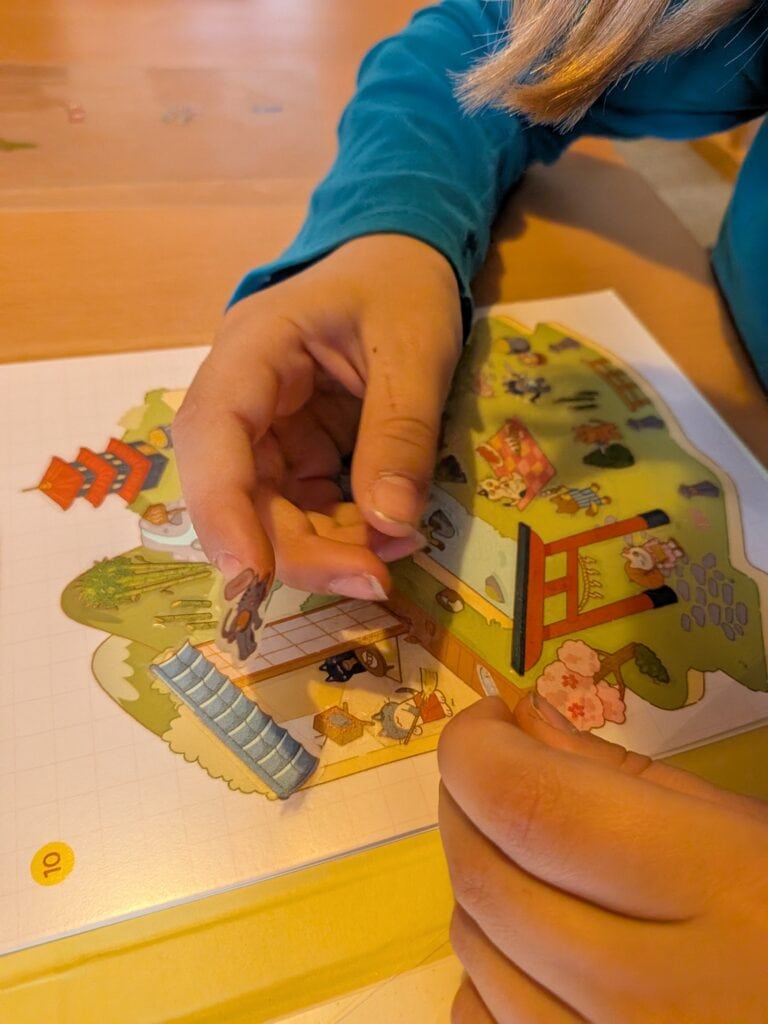 Enfant manipulant une planche de jeu Cosy Cats avec des stickers pour créer une scène ludique.