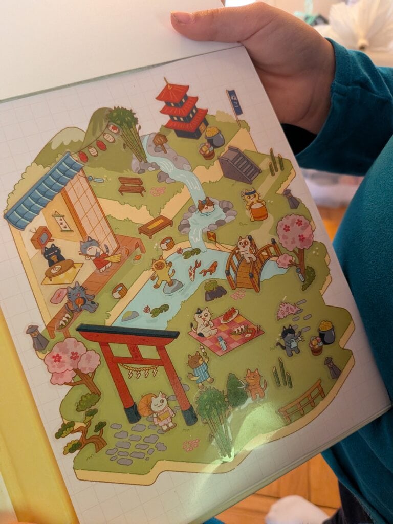 Jeune enfant tenant un livre avec un jeu de stickers illustré d'un parc japonais avec ponts, animaux et structures colorées.