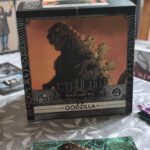 Boîte de jeu Godzilla dans l'extension Cthulhu pour Death May Die, illustrée avec Godzilla et des éléments de monstres mythiques.