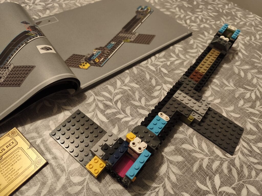 Construction LEGO d'un T-Rex de dinosaures avec pièces colorées sur une table, avec un livre ouvert en arrière-plan.