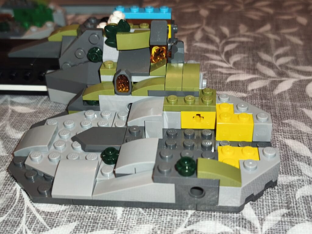 Modèle LEGO représentant un fossile de Tyrannosaurus rex avec détails en gris, vert et jaune, sur une surface en tissu.