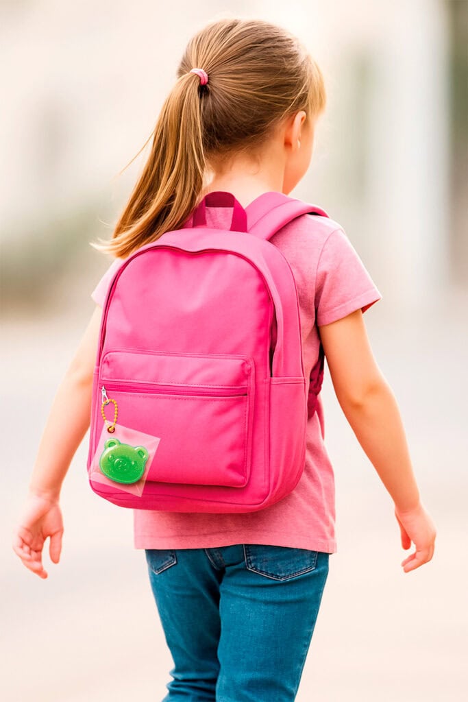 Jeune fille avec un sac à dos rose et un porte-clés en forme de grenouille, vue de dos, en extérieur.