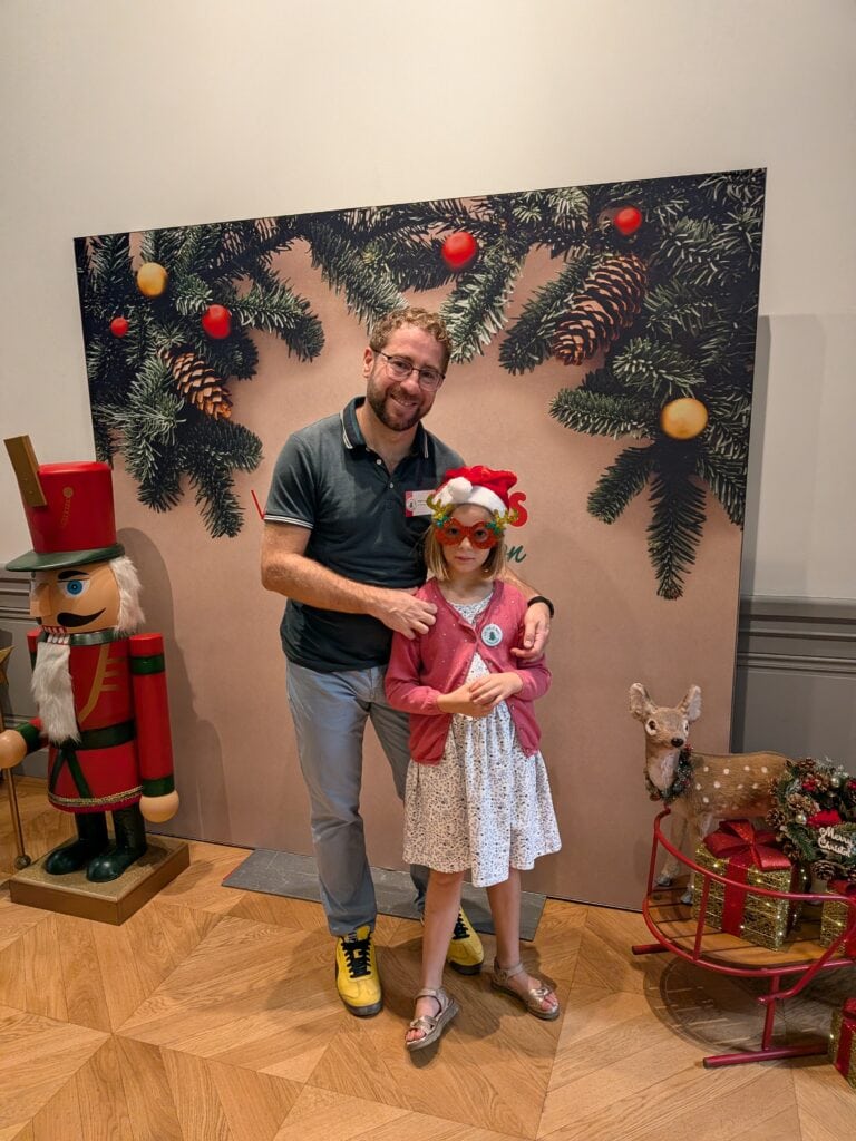 Un homme et une jeune fille posent devant une décoration de Noël avec un sapin, un bonhomme de neige en bois et un renne en peluche.