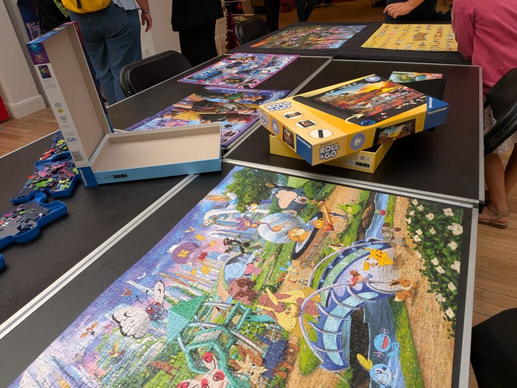 Puzzle coloré représentant un paysage avec des personnages et des animaux, posé sur une table lors d'une réunion de jeux.