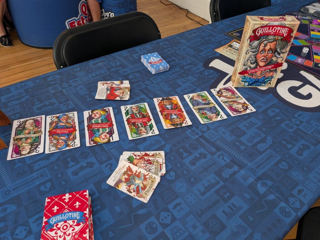 Jeu de société Guillotine avec cartes illustrées sur une table bleue lors d'une session de jeu.