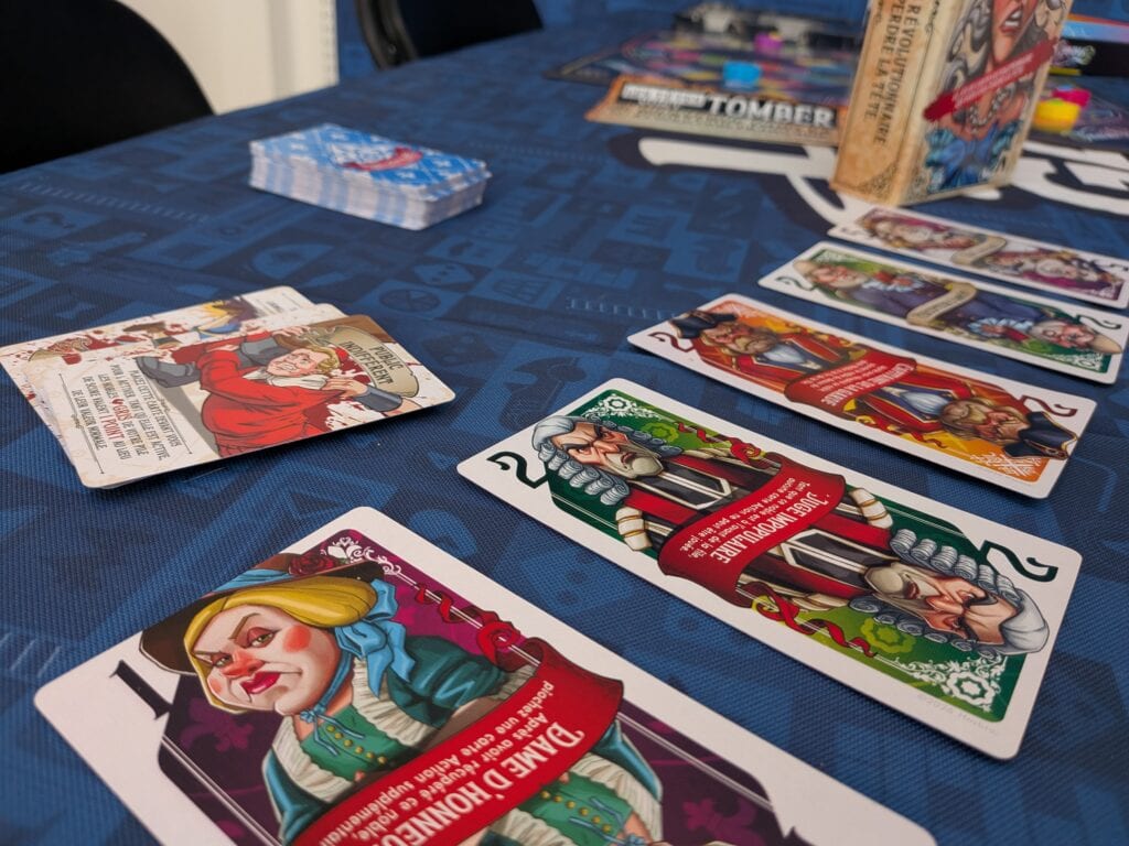 Jeu de cartes de société avec illustrations colorées et personnages variés, posé sur une table bleue lors d'une session de jeu.