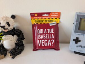 Sac à dos de dossier criminel Pocket avec le titre 'Qui a tué Isabella Vega?' placé entre un robot en LEGO et une console de jeu Nintendo Game Boy.