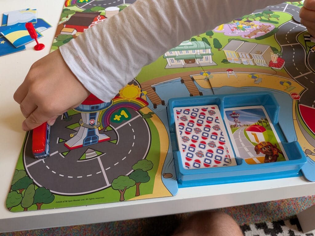 Enfant jouant à un jeu de société coloré avec des pièces et des cartes sur une table.