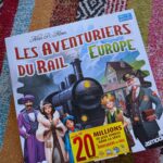 Couverture du jeu de société Les Aventuriers du Rail Europe avec personnages et train sur fond coloré.