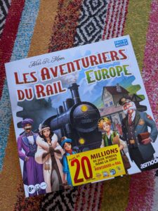 Couverture du jeu de société Les Aventuriers du Rail Europe avec personnages et train sur fond coloré.